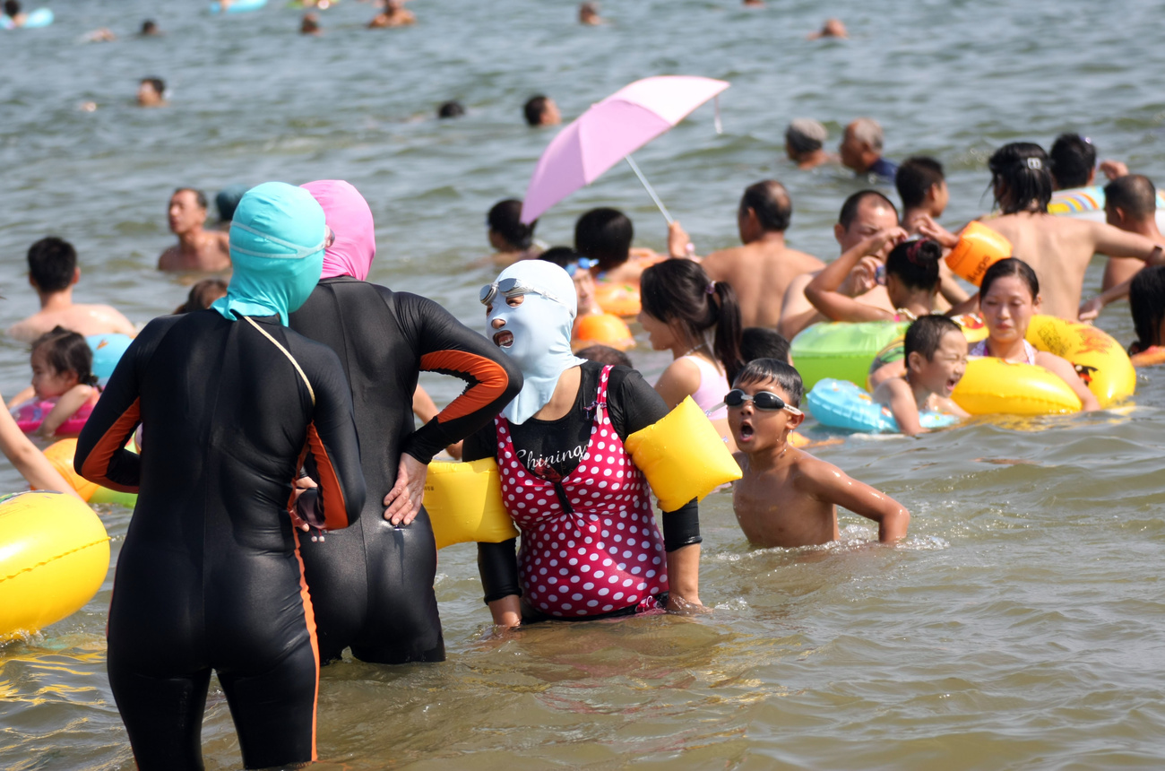 Kínai fürdőzők teljes testet fedő ruhában és arcmaszkban Santung tartomány egyik strandján